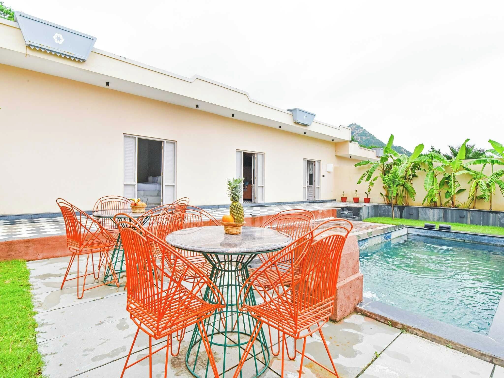 Zona de piscina con mesa y sillas, una piscina pequeña y un edificio con ventanas y una puerta.