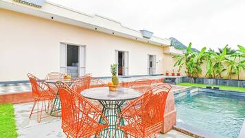 Zona de piscina con mesa y sillas, una piscina pequeña y un edificio con ventanas y una puerta.