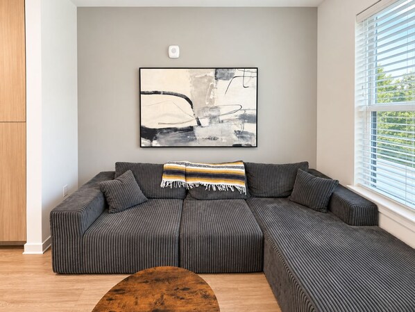 A modern living room with a sectional sofa, a coffee table, and a large abstract painting on the wall.