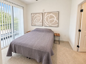 A bedroom with a bed, a small table, two abstract paintings, and a door.