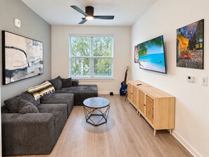A modern living room with a sectional sofa, a round coffee table, a wooden cabinet, and artwork on the walls.