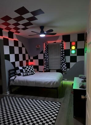 Un dormitorio con piso a cuadros, una cama con almohadas a cuadros, un ventilador de techo y una pared con estampado de cuadros.