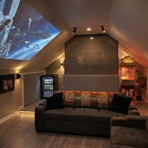 Una habitación acogedora con una pantalla grande mostrando una escena espacial, una máquina de palomitas de maíz y un sofá con una manta.