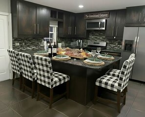 Una cocina con armarios de madera oscura, encimera de granito y una isla central con sillas a cuadros.