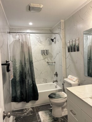 Ein Badezimmer mit Duschvorhang, Toilette, Badewanne und Waschtisch mit Spiegel.