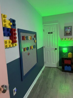A hallway with a pegboard wall, a door, and a small table with a lamp. - The Grandstand Getaway (Blakeslee)