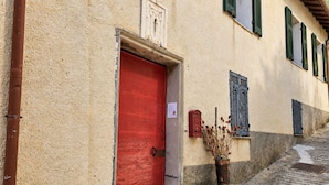 Un edificio con puerta roja, contraventanas verdes y una escalera de piedra que conduce a la entrada.