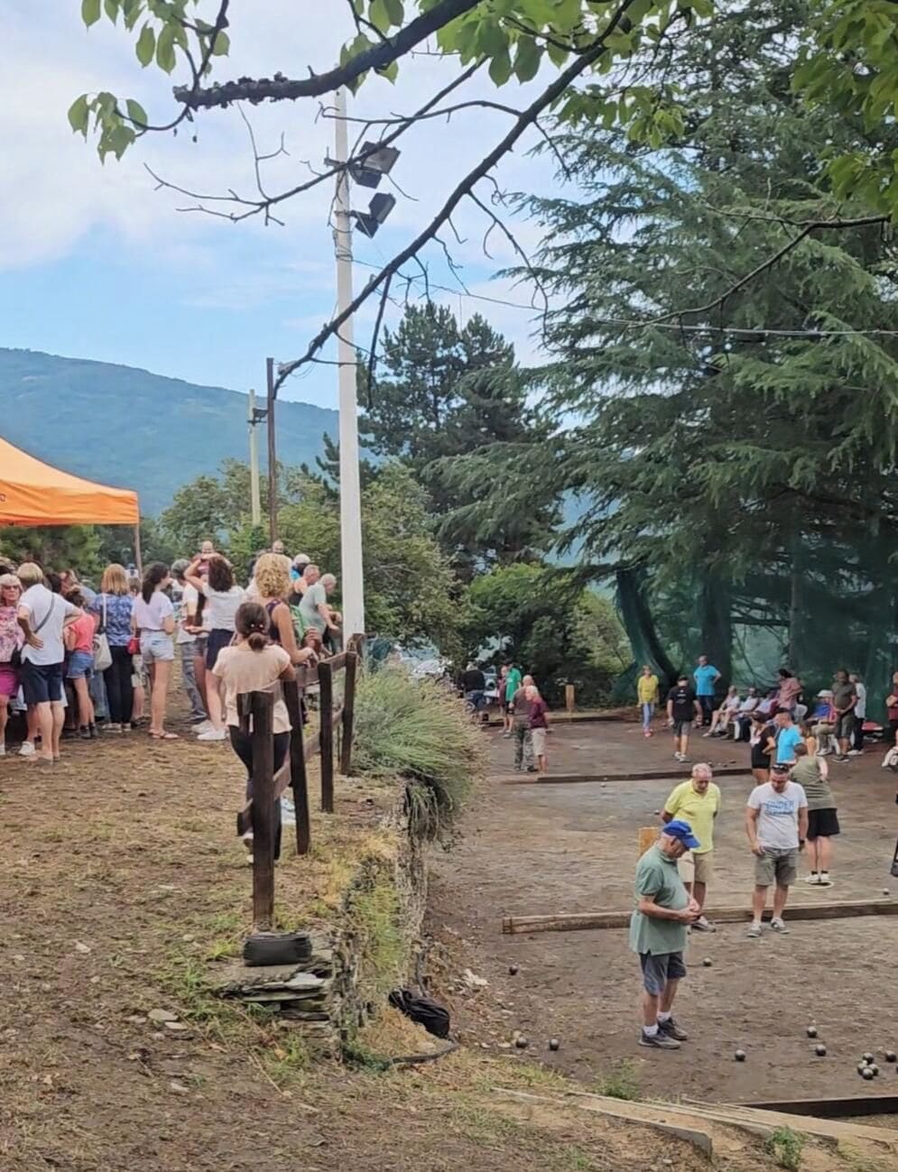 Un'area esterna con terreno sterrato, una recinzione in legno e un gruppo di persone riunite vicino a un albero.