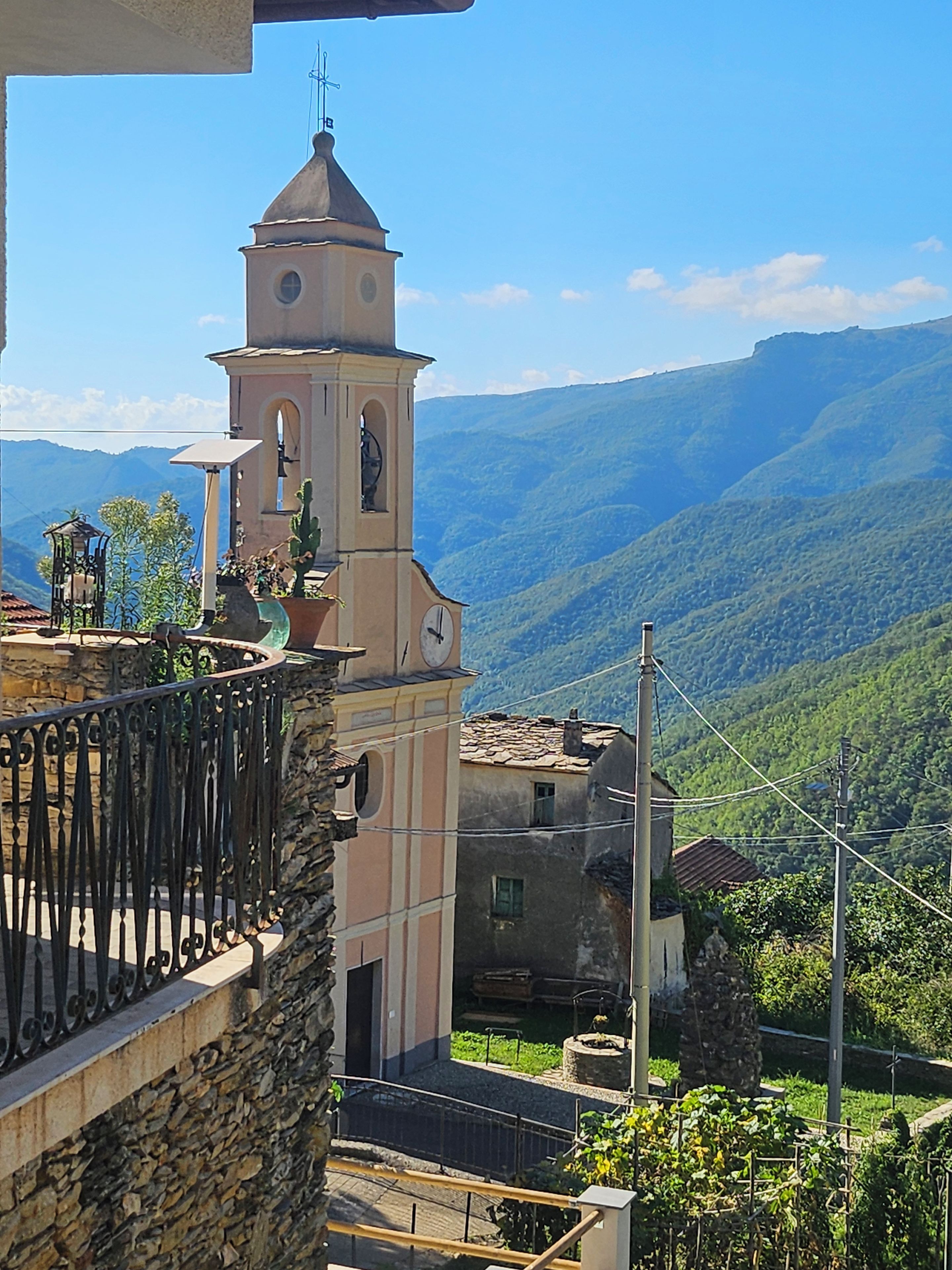 A building with a bell tower, stone walls, and a view of green hills.