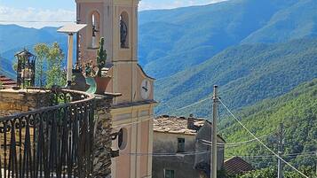 A building with a bell tower, stone walls, and a view of green hills.
