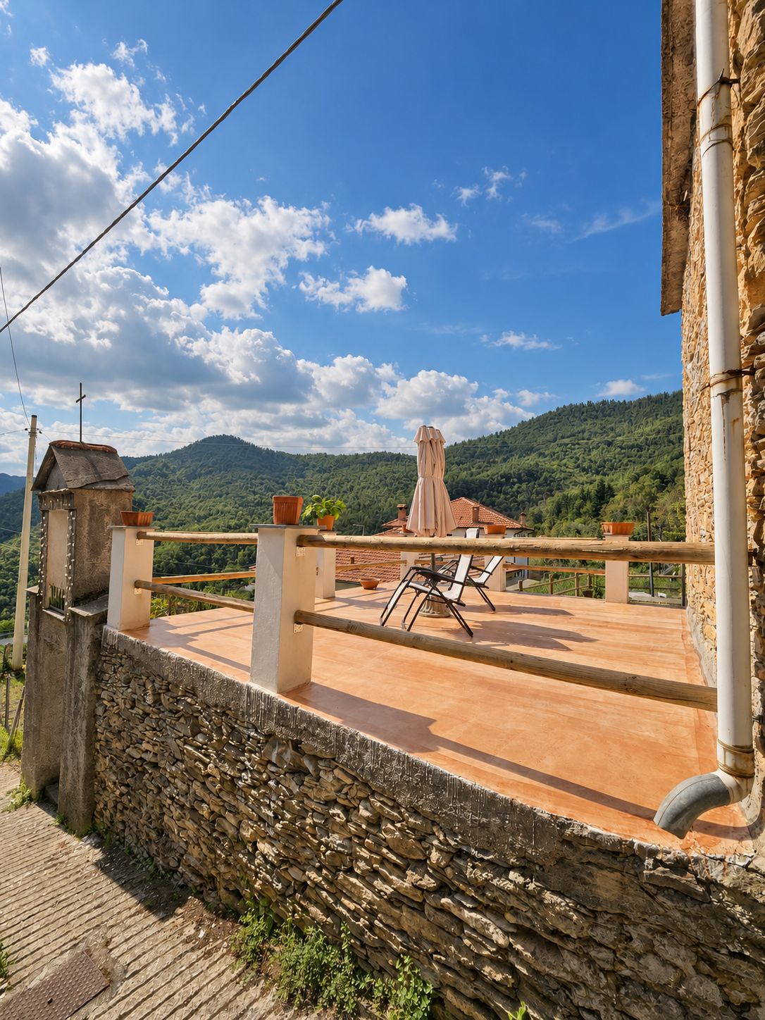 Un mur de pierre, une terrasse avec une table et des chaises, et une vue sur une montagne.