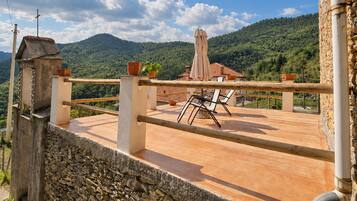 Un mur de pierre, une terrasse avec une table et des chaises, et une vue sur une montagne.
