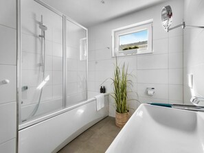 Ein modernes Badezimmer mit Duschkabine aus Glas, einer weißen Badewanne und einem kleinen Fenster mit Blick.