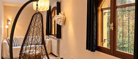 Une pièce avec un fauteuil suspendu, un radiateur, une fenêtre avec des rideaux et un luminaire fixé au mur.