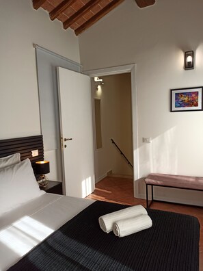 A hotel room with a bed, a bench, a nightstand with a lamp, a door leading to a staircase, and a framed picture on the wall. - Gora XV Segreto - House on the Water in the Center of Colle Val d'Elsa (Colle di Val d'Elsa)