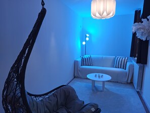 Une pièce comprenant un fauteuil suspendu, un canapé, une petite table ronde et un lampadaire.