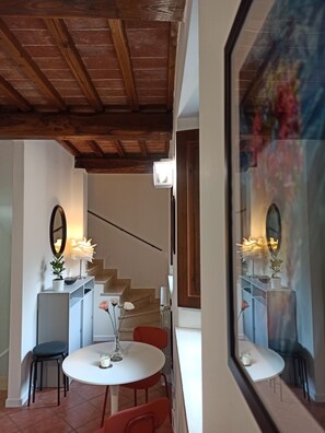 Un coin repas avec une table ronde, des chaises, un miroir et un escalier en arrière-plan.