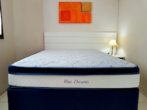 Een bed met een gewatteerd matras, voorzien van de aanduiding 'Blue Dreams', en een nachtkastje met een lamp.