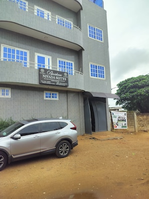 A multi-story building with a sign for 'Nivada Suites' indicating it is a hotel. There is a parked car in front.