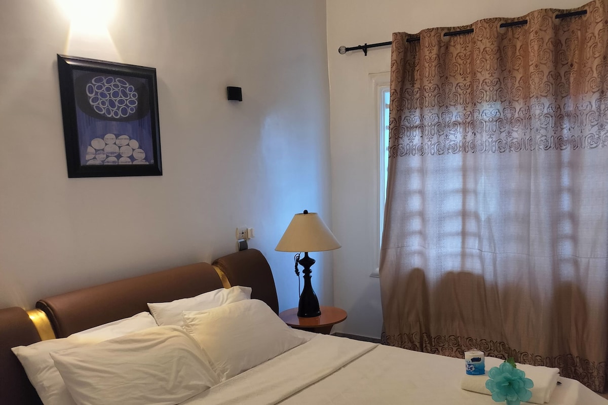 Een net opgemaakt bed met witte lakens, een bedlamp en een decoratief kussen.