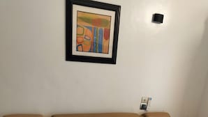 A hotel room with a bed, pillows, a framed artwork on the wall, and a wall-mounted control panel. - Résidence Nivada Suite (Porto-Novo)