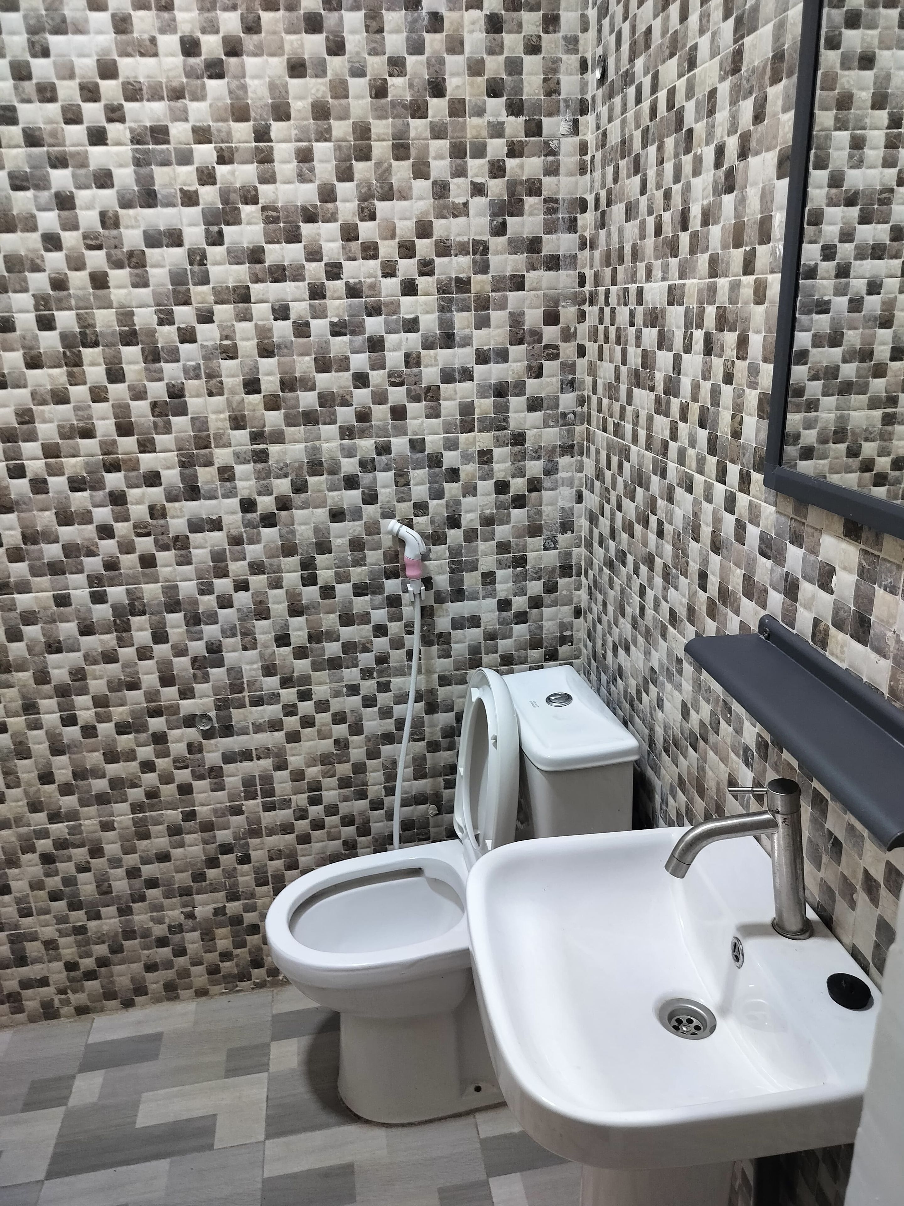 Ein Badezimmer mit mosaikbesetzter Fliesenwand, Toilette, Waschbecken und Spiegel.