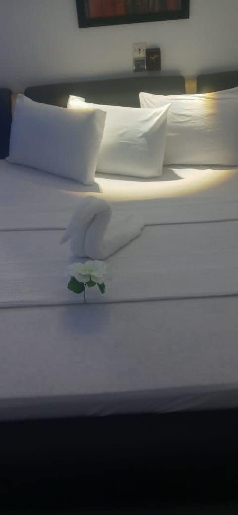Una cama bien hecha con sábanas blancas, una toalla doblada y una pequeña flor blanca.