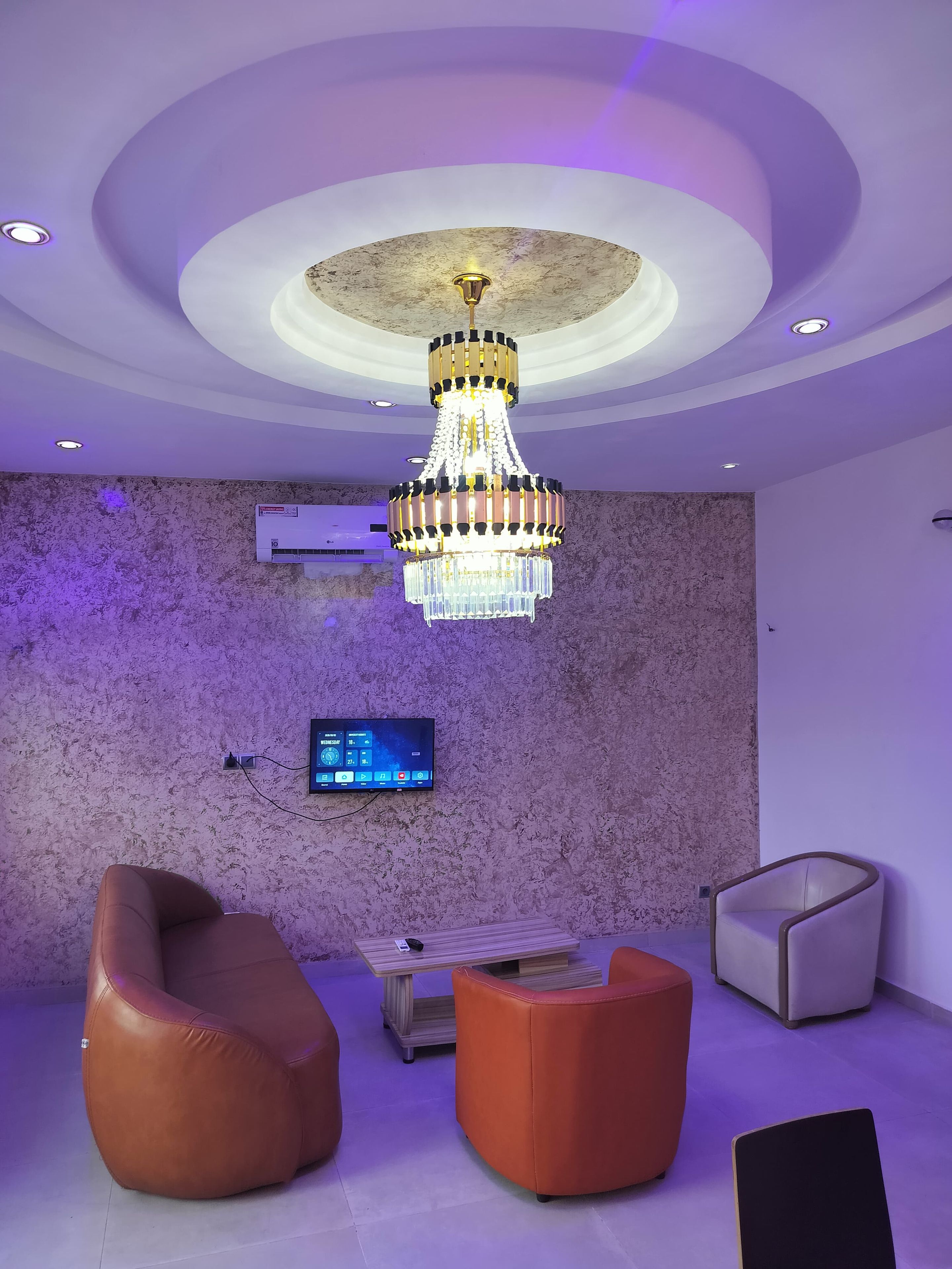 A modern interior with a chandelier, leather seating, a flat-screen TV, and a marble wall.