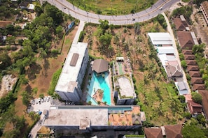 Ein Hochhaus mit Pool auf dem Dach, umgeben von Grünflächen und einer gewundenen Straße.