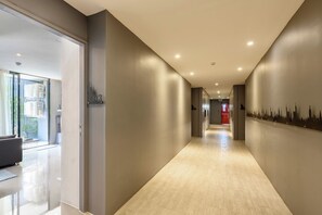 Een moderne hotelgang met een glazen deur, een gang met een muurschildering van de stadshemel en een rode deur aan het einde.