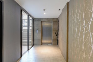 Ein Flur mit Glastür zu einer Treppe, einem an der Wand montierten Rauchmelder und einer strukturierten Wandgestaltung.