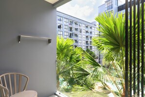 Een balkon met een stoel, een metalen hekwerk en uitzicht op een gebouw met meerdere ramen en palmbomen.