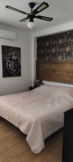 A bedroom with a bed, a ceiling fan, a wall-mounted air conditioner, a motorcycle poster, and a wooden headboard. - House for 4–6 people in Torrevieja (Torrevieja)