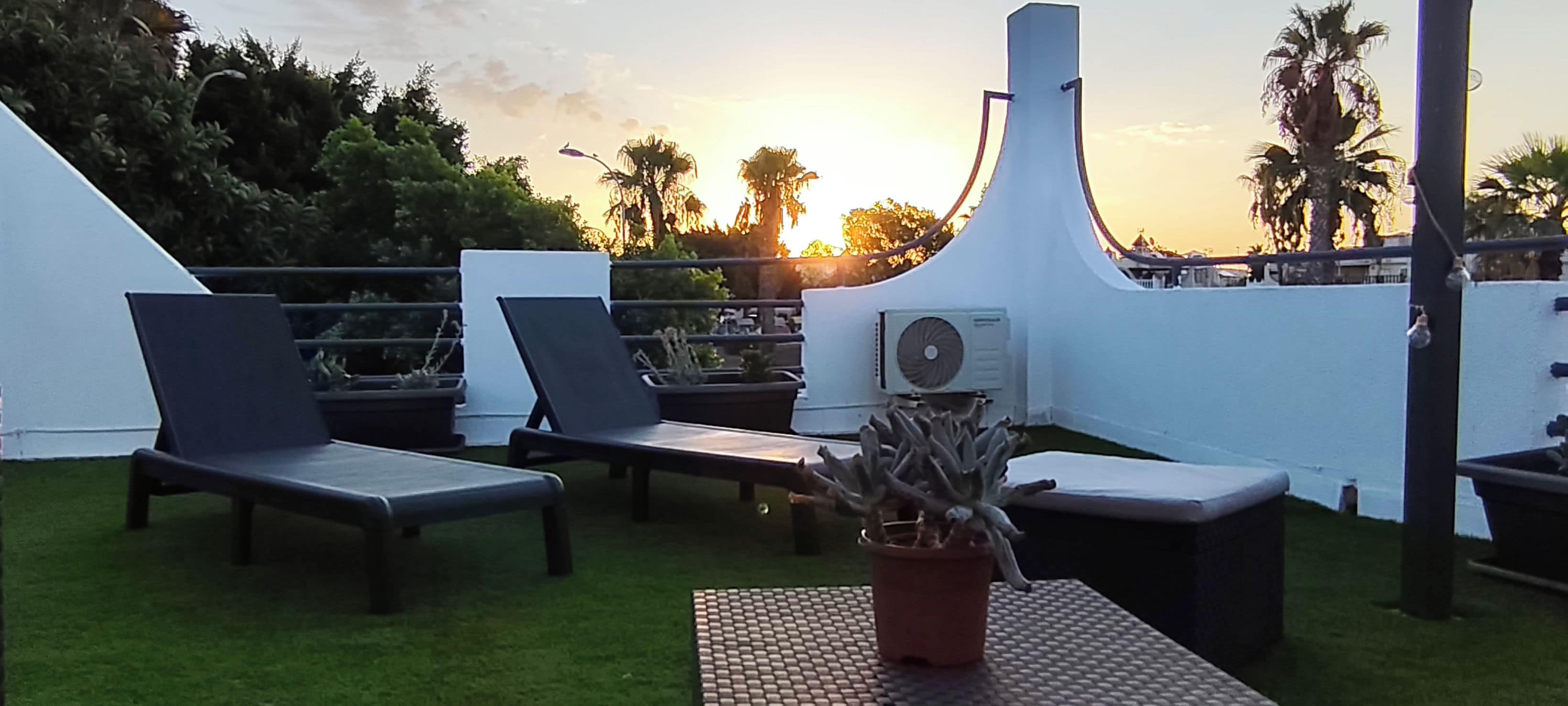 A rooftop terrace with lounge chairs, a potted plant, and an air conditioning unit.