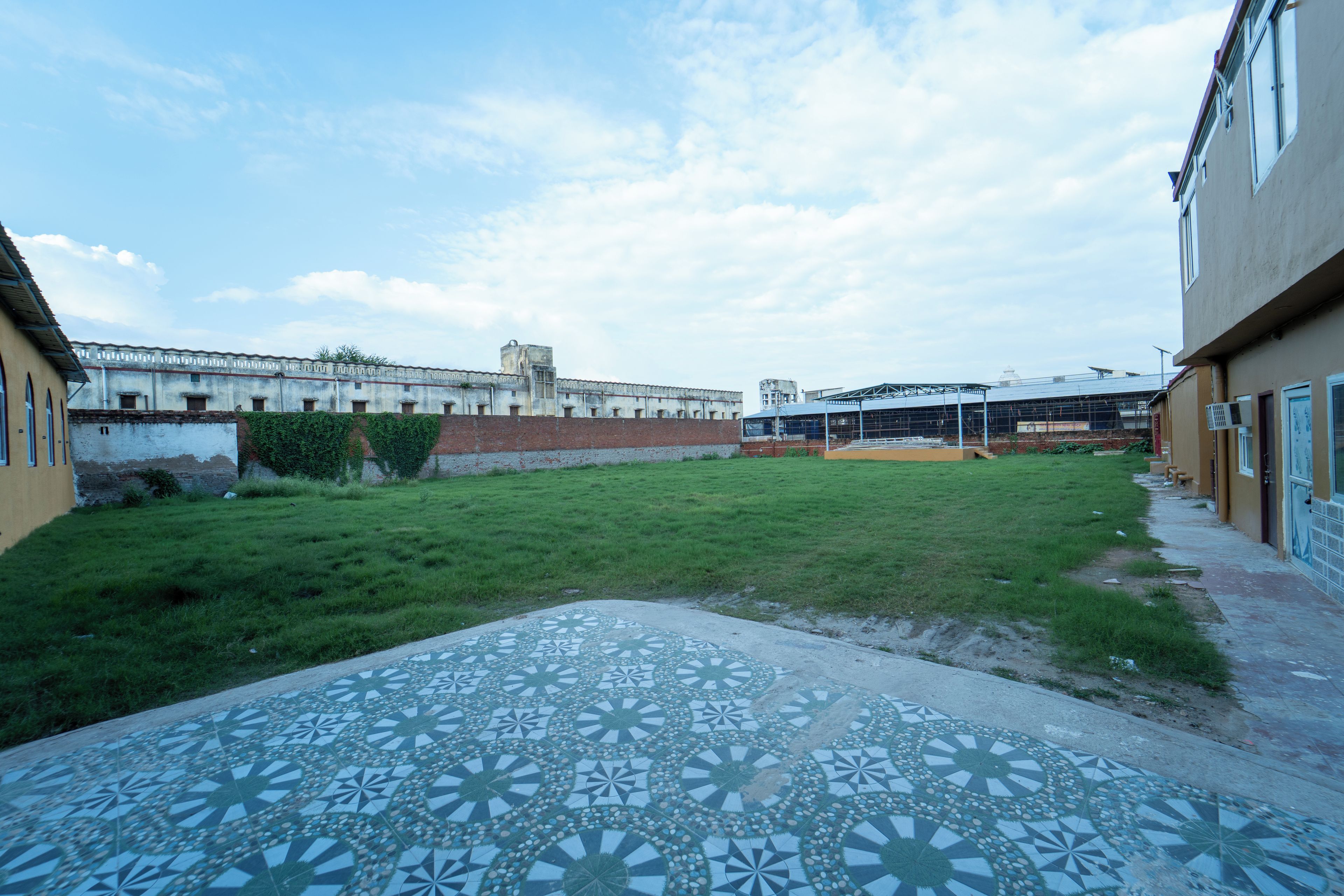 A courtyard with a patterned pavement, a brick wall, and a building with a flat roof.