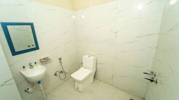 A bathroom with white marble walls, a white sink, a toilet, and a shower.