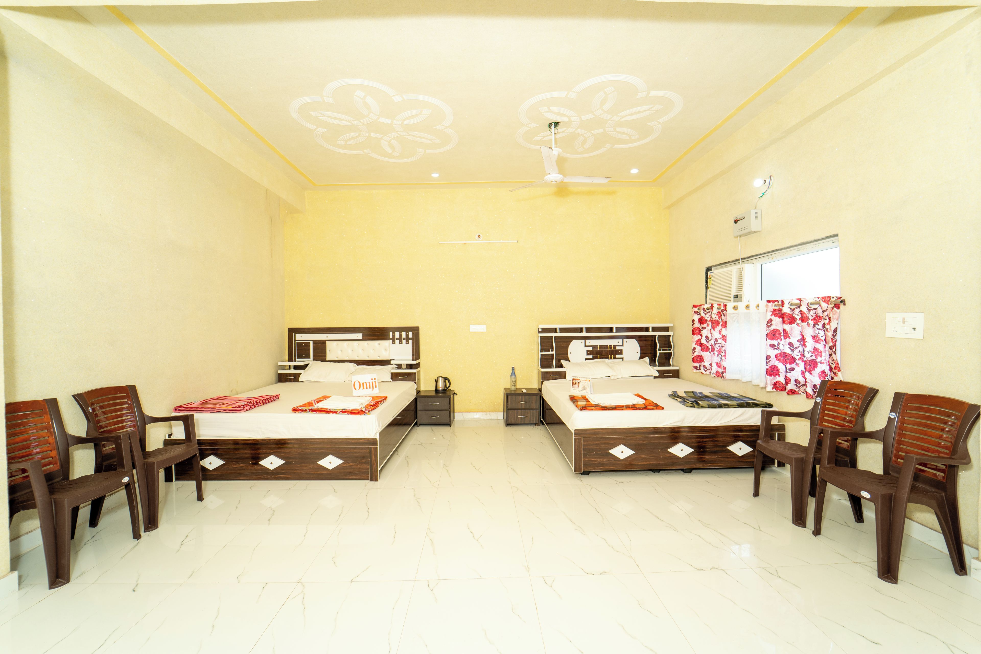 A hotel room with two beds, a ceiling fan, a window with curtains, and a tiled floor.