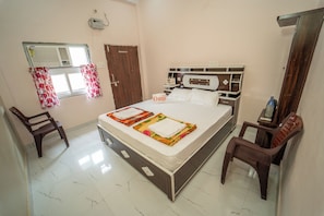Une chambre d’hôtel comprenant un lit, deux chaises, une table de chevet, une fenêtre avec des rideaux et un climatiseur fixé au mur.
