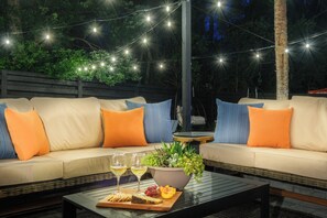 Un espace extérieur aménagé avec un canapé, des coussins, une table avec des verres et des collations, et des guirlandes lumineuses.