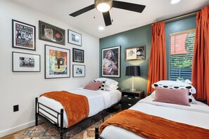 Ein Hotelzimmer mit zwei Betten, einem Deckenventilator, gerahmten Bildern an der Wand und einem Fenster mit Vorhängen.