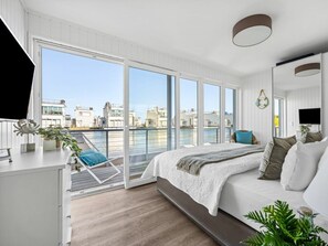 Ein modernes Schlafzimmer mit großem Fenster, einem Bett, einem Schreibtisch und einem Sessel.
