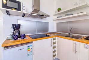 Eine kompakte Küche mit integrierter Kaffeemaschine, einer Mikrowelle und einem kleinen Kühlschrank.