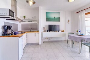 A compact kitchen with a microwave, kettle, and coffee maker, a dining area with a table and chairs, and a large window with a view of the sea. - Apartamento Delphin Sol – Sea Views and Beachfront Location in Puerto Naos (Puerto de Naos)