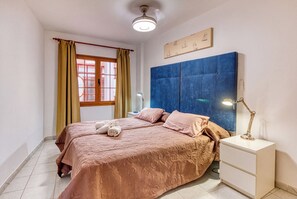 A bedroom with a bed, a nightstand, a lamp, a window with curtains, and a wall with a framed picture. - Apartamento Delphin Sol – Sea Views and Beachfront Location in Puerto Naos (Puerto de Naos)