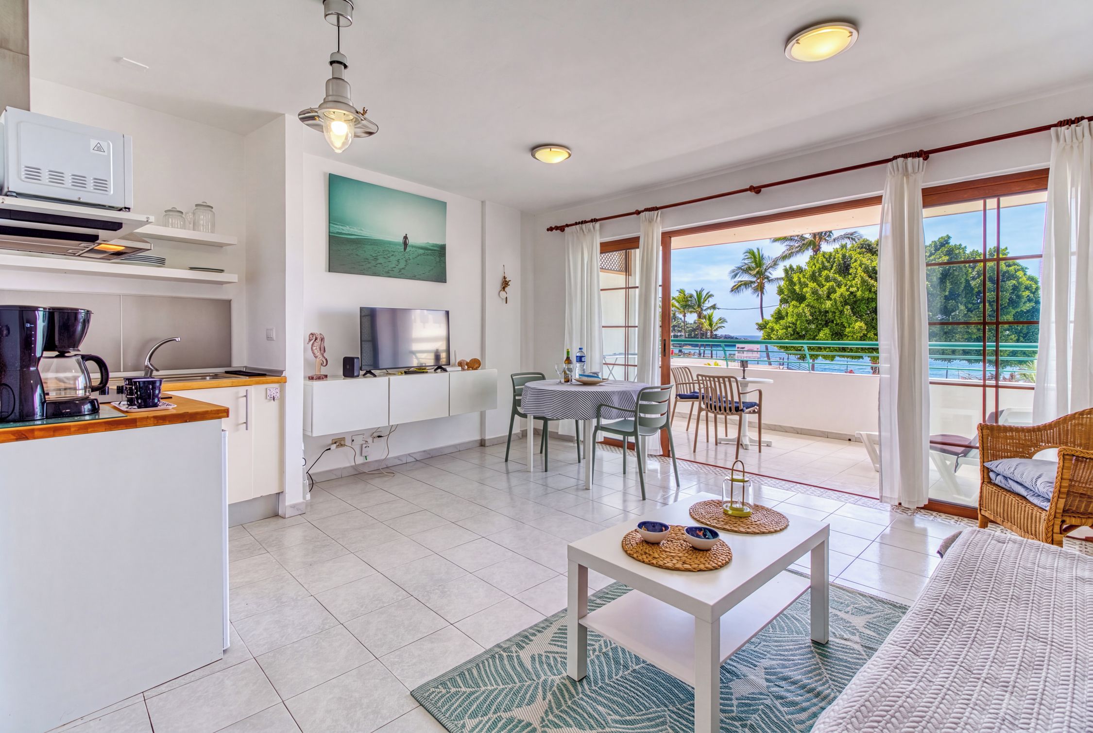 Een moderne keuken met een koffiezetapparaat, een eethoek met een tafel en stoelen, en een balkon met uitzicht op de oceaan.