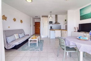 A compact living space with a sofa, dining table, kitchenette, and a television. - Apartamento Delphin Sol – Sea Views and Beachfront Location in Puerto Naos (Puerto de Naos)