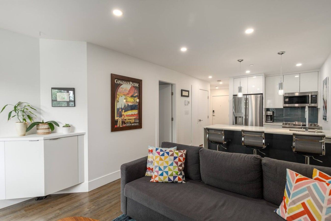 A modern apartment with a grey sofa, a kitchen with stainless steel appliances, and a poster on the wall.