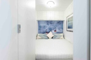 Ein Schlafzimmer mit einem Bett, einem Kopfteil mit Himmel und Seilbahn-Motiv und einem weißen Kleiderschrank.