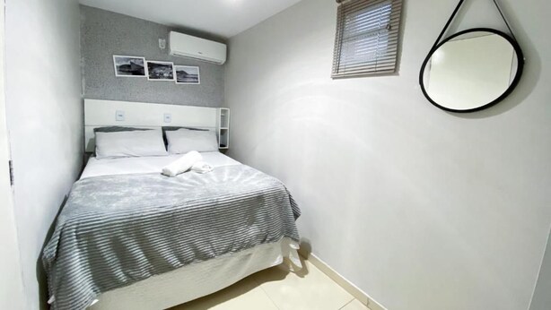 A bedroom with a bed, a round mirror, and a window with blinds. - Hospedaria Valdice Damasceno (Piranhas)