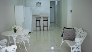 A compact living space with a kitchenette, a dining table with chairs, and a white sofa. - Hospedaria Valdice Damasceno (Piranhas)
